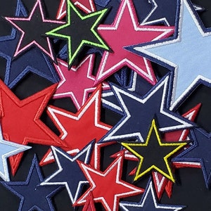 Puede incluir: Una colección de parches con forma de estrella de colores con contornos blancos. Los parches están hechos de tela y tienen una variedad de colores, incluyendo rojo, azul, rosa y verde.