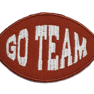 May include: A brown felt football-shaped patch with white embroidered text that reads "GO TEAM".