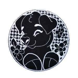 May include: Black and white embroidered patch of a cartoon dog with a winking eye and flowers around it.