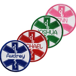 Puede incluir: Cuatro parches redondos blancos bordados con un símbolo de estrella de la vida rojo, verde, azul y rosa. Cada parche tiene un nombre: Audrey, Michael, Joshua y Jenn.
