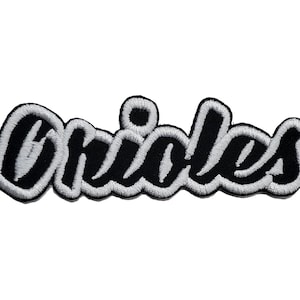 May include: Black and white embroidered patch with the word "Orioles" in a stylized font.