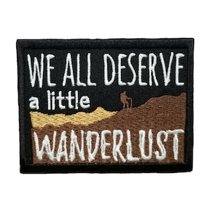Könnte beinhalten: Schwarzer gestickter Aufnäher mit weißem Text, der "We all deserve a little wanderlust" lautet. Der Aufnäher zeigt eine braune und gelbe Landschaft mit einer kleinen Silhouette einer Person, die auf einem Hügel steht.