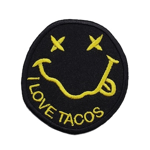 Puede incluir: Parche bordado negro con una cara sonriente amarilla y el texto "I LOVE TACOS" alrededor del borde.