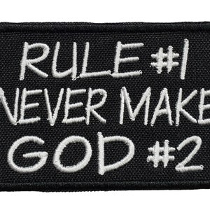 以下が含まれることがあります： 「RULE #1 NEVER MAKE GOD #2」と白文字で書かれた黒い刺繍パッチです。