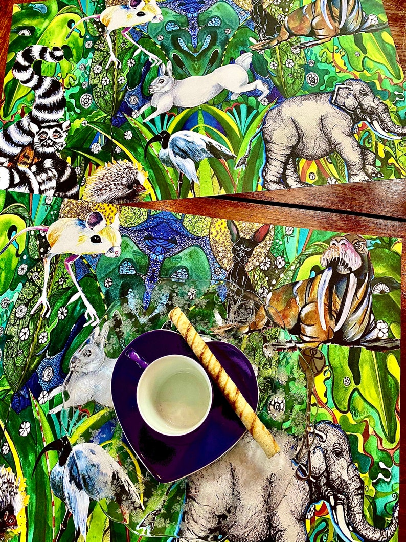 May include: Two placemats with a colorful jungle animal print design. The placemats feature a variety of animals, including elephants, mice, birds, and a rabbit. A purple heart-shaped saucer with a white teacup and a long, thin, brown cookie sits on top of the placemats.