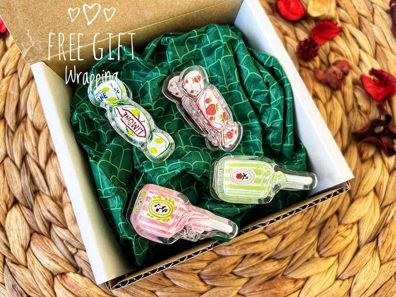 May include: A gift box with four clear acrylic candy-shaped charms. The charms include a strawberry, a lemon, and a bottle design. The box is lined with green patterned tissue paper. The text "FREE GIFT Wrapping" is visible on the box.