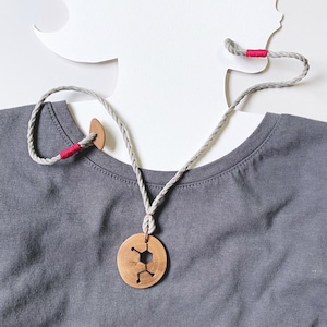May include: A gray t-shirt with a wooden necklace featuring a geometric design. The necklace is made of a natural rope and has a wooden pendant.