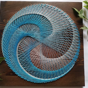 Puede incluir: Una pieza circular de arte de cuerda con un diseño azul y blanco. El arte de cuerda está montado en un marco de madera marrón oscuro.