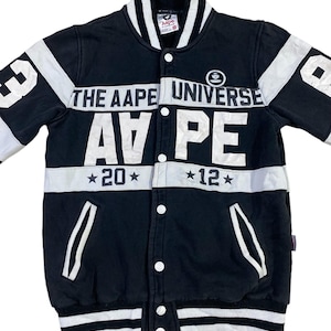 May include: Black and white varsity jacket with the words "The Aape Universe" and "Aape" in white lettering. The jacket has white stripes on the sleeves and bottom hem. The jacket has a button closure.