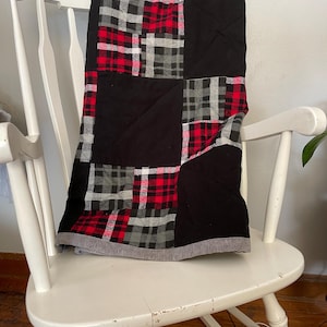 Może przedstawiać: Czarno-czerwono-biała pikowana kołdra w kratę z szarym obramowaniem. Kołdra jest złożona i leży na białym bujanym krześle.