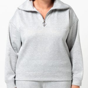 May include: A light gray sweatshirt and matching sweatpants set. The sweatshirt features a high collar, a silver zipper, and a horizontal seam across the chest. The outfit appears to be made of a soft, comfortable material, suitable for casual wear.