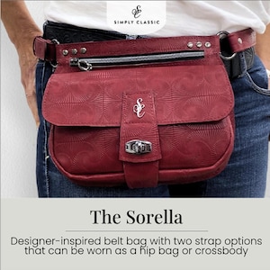 May include: A burgundy belt bag with a textured pattern, worn around the waist. The bag has a silver zipper, a flap with a silver clasp, and a decorative silver emblem. The belt is black with silver studs. The bag is labeled "The Sorella".