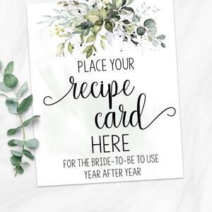 May include: A printable sign with a watercolor floral design in shades of green and white. The sign says "Place your recipe card here for the bride-to-be to use year after year".