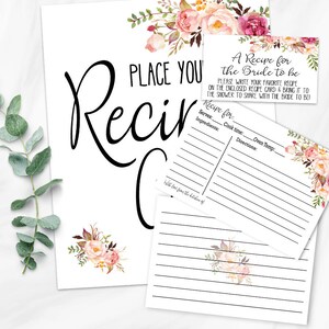 May include: White recipe cards and sign with floral accents. The sign reads "Place Your Recipe" in large black script. Smaller cards say "A Recipe for the Bride to be" and provide space for recipe details. Floral bouquets in pink and burgundy adorn the cards.