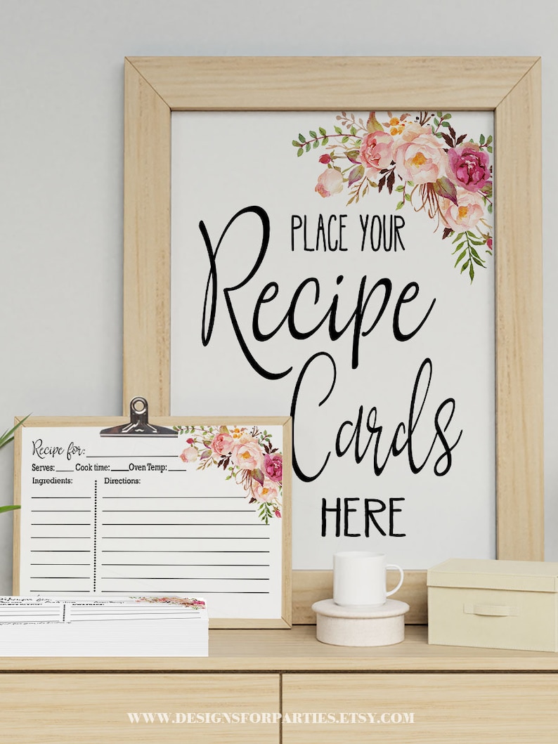 May include: A framed sign with the text "PLACE YOUR Recipe Cards HERE" and a floral design. A smaller recipe card holder and a stack of recipe cards are in front. The design includes a white mug and a small box.