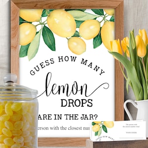 May include: A framed sign with a watercolor lemon design and the text "Guess How Many Lemon Drops Are in the Jar?" A jar of yellow candies and a small card with the text "Your Guess" are also visible.