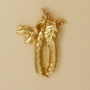 May include: A gold charm in the shape of two pea pods with leaves. The charm is made of solid gold and has a detailed design.