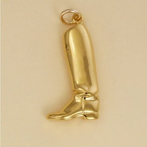 Puede incluir: Un colgante de bota de color dorado. La bota está detallada con una punta puntiaguda y una parte superior plegable.