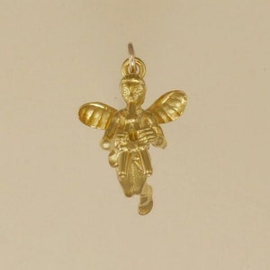 May include: Gold-toned angel charm with wings outstretched, playing a flute. The angel is wearing a flowing robe and has a serene expression.