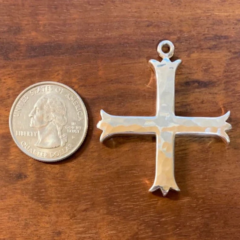 Pu&ograve; includere: Un ciondolo a forma di croce in argento con una texture martellata. La croce &egrave; circa delle dimensioni di una moneta da un euro.