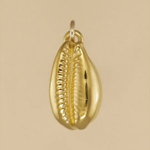 Puede incluir: Un colgante de concha de cauri de color dorado. La concha es detallada y realista.