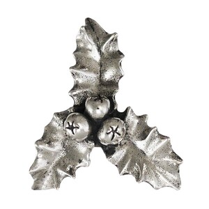 May include: A silver-coloured holly leaf and berry ornament. The ornament features three leaves and three berries. The berries have a star-like design. The leaves have a textured surface. The ornament is likely for festive decor.