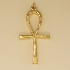 May include: A gold-coloured Ankh pendant with a hammered texture. The Ankh is an ancient Egyptian symbol of life.