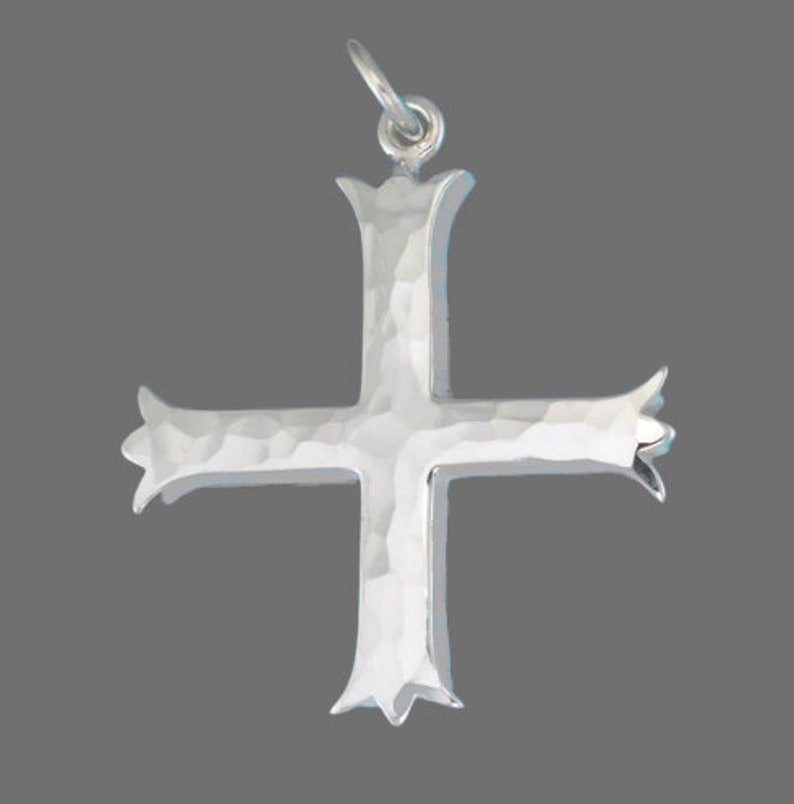 Pu&ograve; includere: Un ciondolo a forma di croce in argento con una texture martellata. La croce ha un design semplice ed elegante con una parte superiore e inferiore leggermente ornata.