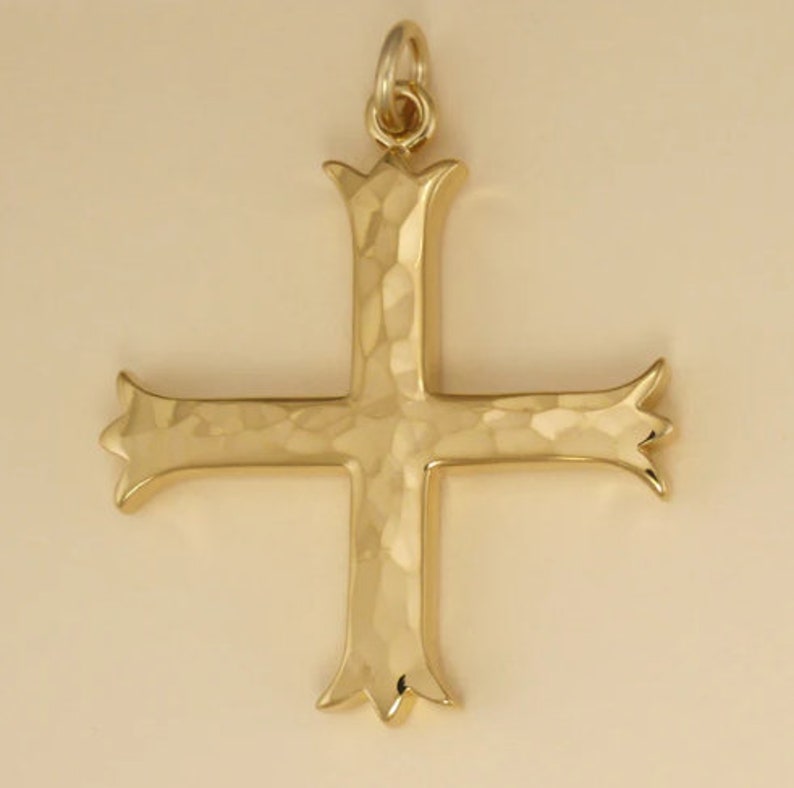 Pu&ograve; includere: Un ciondolo a forma di croce martellato color oro con un design decorativo. La croce &egrave; un simbolo religioso spesso utilizzato nei gioielli.