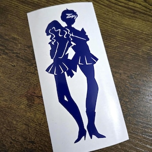 May include: A blue vinyl sticker featuring two stylized figures in sailor-style outfits. The figures are posed together, with one figure's arm around the other. The sticker is on a white background.