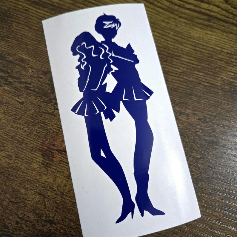May include: A blue vinyl sticker featuring two stylized figures in sailor-style outfits. The figures are posed together, with one figure's arm around the other. The sticker is on a white background.