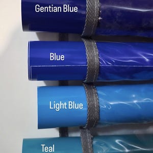 May include: Four rolls of blue vinyl material in varying shades, including Gentian Blue, Blue, Light Blue, and Teal. Each roll is secured with a gray strap and labeled with its color name.