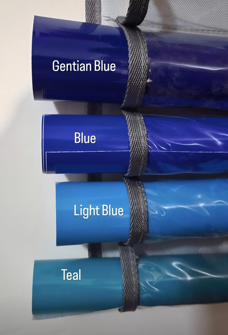 May include: Four rolls of blue vinyl material in varying shades, including Gentian Blue, Blue, Light Blue, and Teal. Each roll is secured with a gray strap and labeled with its color name.