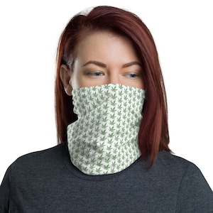 May include: A white face covering with a repeating pattern of green cannabis leaves. The face covering is worn around the neck and covers the lower face.
