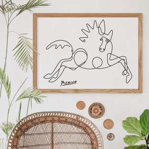 May include: A black and white line drawing of a horse by Pablo Picasso in a wooden frame. The artwork is hanging on a white wall above a wicker chair.
