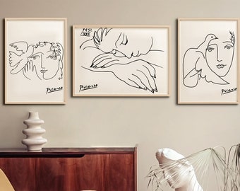 May include: Three black and white line drawings of a woman's face with a dove. The drawings are framed in light wood and hung on a light beige wall. The drawings are by Pablo Picasso and include his signature.