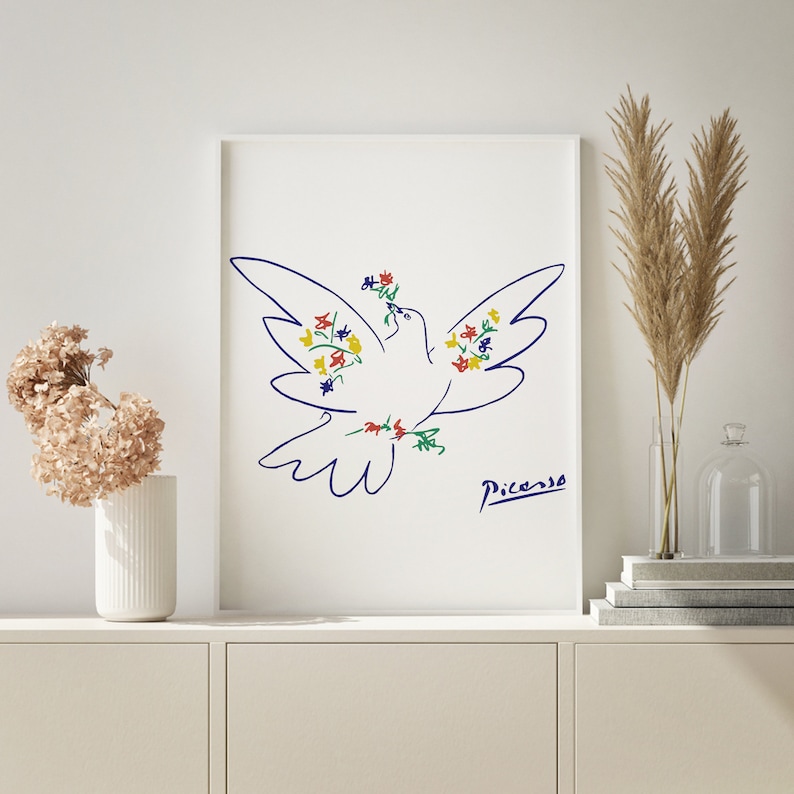May include: A white framed print of a blue line drawing of a dove with colorful flowers. The dove is flying with its wings spread and has a flower in its beak. The artist's signature, "Picasso", is in the bottom right corner.