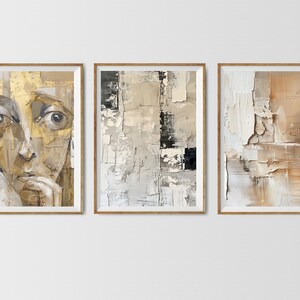 May include: Three framed abstract paintings in muted tones of brown, beige, and white. The leftmost painting features a close-up of a person's face with a contemplative expression. The middle painting is a geometric abstract design with a black rectangle in the center. The rightmost painting is a textured abstract design with a more organic feel.