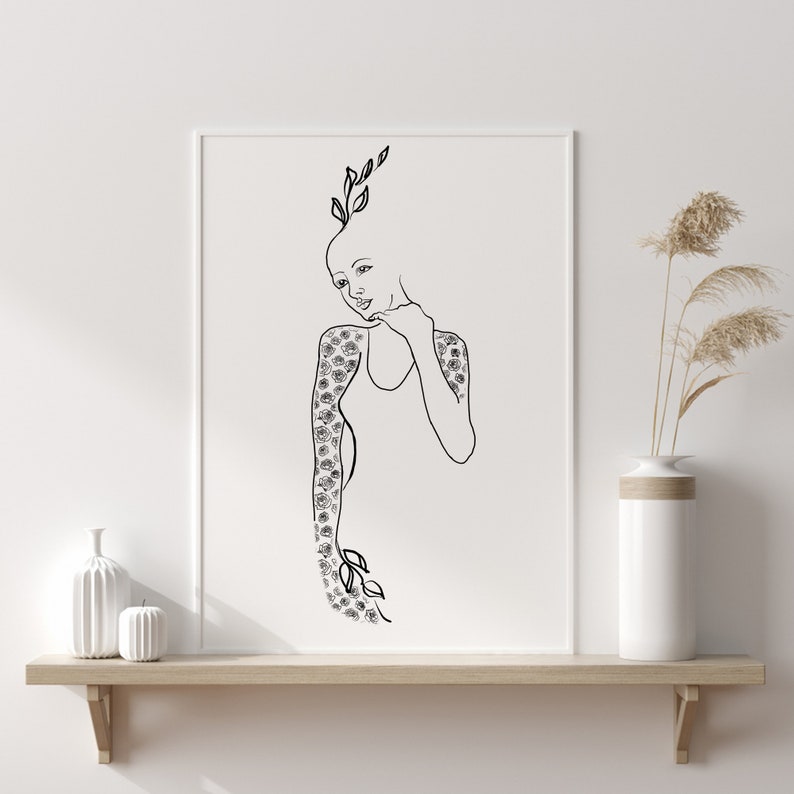 Op de afbeelding: Zwart-witte lijntekening van een vrouw met bloemen die uit haar lichaam groeien. De print is ingelijst en hangt aan een witte muur boven een houten plank.