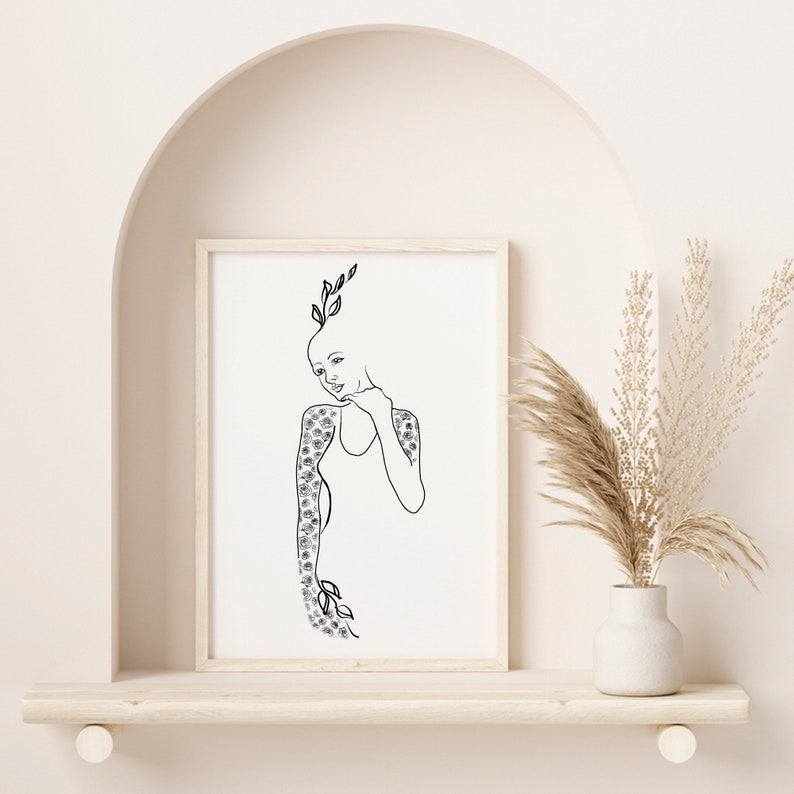 Op de afbeelding: Een zwart-witte lijntekening van een persoon met bloemen die uit hun lichaam groeien. De tekening is ingelijst en hangt aan een muur.