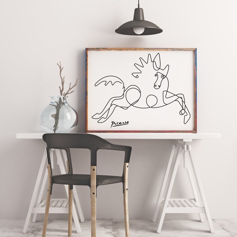 May include: A black and white line drawing of a horse, with the signature "Picasso" below the image. The drawing is framed in a brown wood frame and is hanging on a white wall.