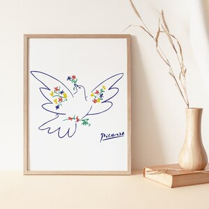 May include: A framed print of a white dove with blue outlines, holding a bouquet of colorful flowers in its beak. The dove is drawn in a simple, minimalist style, reminiscent of Pablo Picasso's work. The print is signed "Picasso" in the bottom right corner.