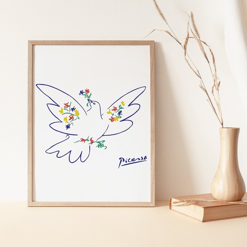 May include: A framed print of a white dove with blue outlines, holding a bouquet of colorful flowers in its beak. The dove is drawn in a simple, minimalist style, reminiscent of Pablo Picasso's work. The print is signed "Picasso" in the bottom right corner.