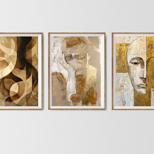 May include: Three framed abstract art prints with gold and brown tones. The first print features geometric shapes, the second print features a portrait of a person with a hat, and the third print features a portrait of a person with a gold background.