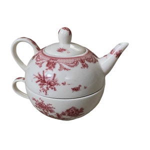 May include: A white teapot and cup set with a red floral pattern. The teapot has a lid and a handle. The cup has a handle and is sitting inside the teapot.