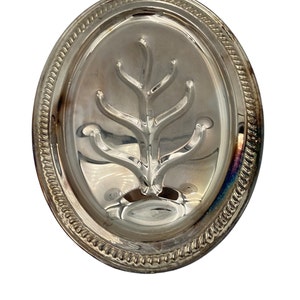 May include: A silver-coloured, oval serving tray with a tree-like design in the centre. The tray has a decorative, beaded edge. The reflective surface of the tray creates highlights and shadows.