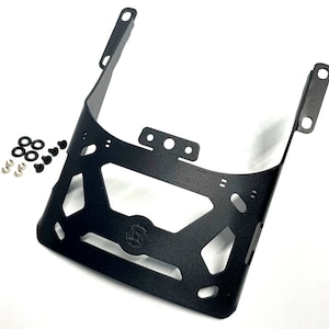 May include: Black metal motorcycle luggage rack with mounting hardware. The rack has a rectangular shape with cutouts and a logo in the centre.