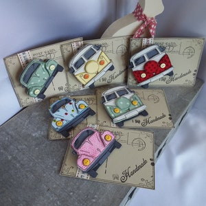 May include: Six handmade vintage camper van pins on postcard backgrounds. The vans are decorated with different patterns and colours, including green, red, yellow, blue, and pink. Each pin has a "Handmade" label.
