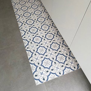 Op de afbeelding: Een gepatenteerde vloermat met een geometrisch ontwerp in blauw, grijs en wit. De mat ligt op een grijze tegelvloer.