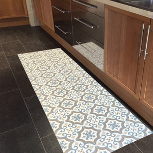 May include: A patterned kitchen rug with a blue, brown, and white geometric design. The rug is placed in front of a set of kitchen cabinets.